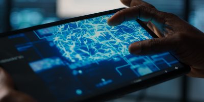 Close up of computer scientist in data center uses AI on tablet, verifying compliance of racks. IT expert using artificial intelligence on device to optimize resource utilization, camera A